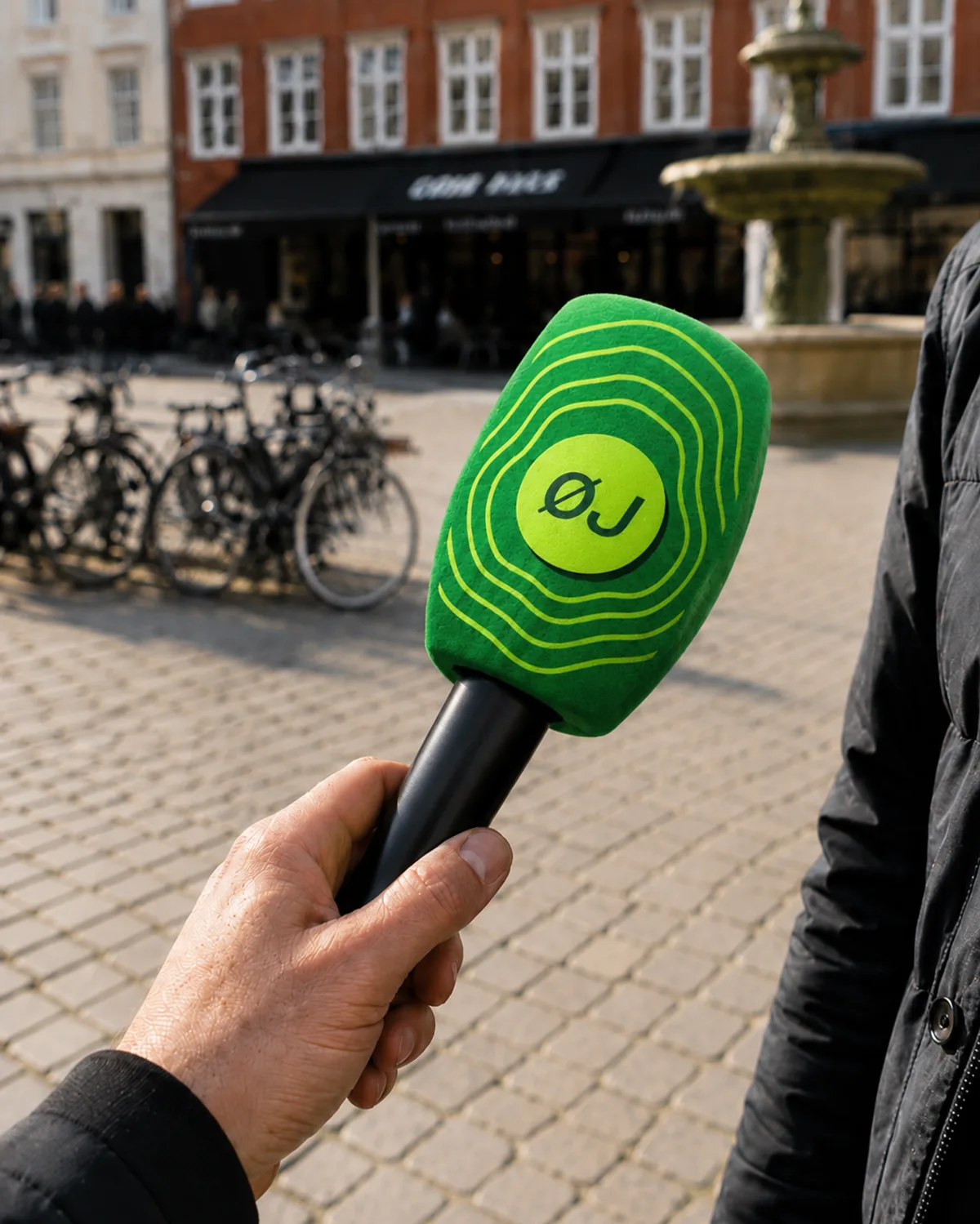 Mikrofon med ØJ-logoknappen og pulsringene — identiteten ude i verden